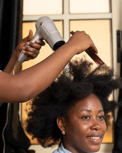Brushing au sèche-cheveux sur cheveu naturel, cliente souriante